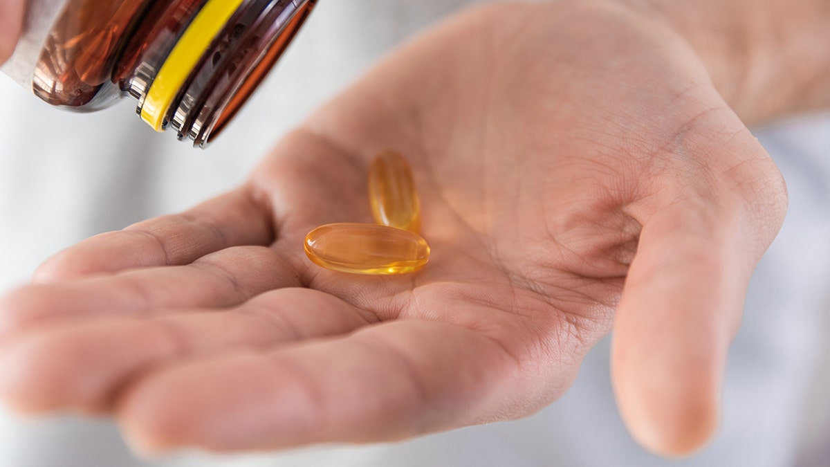 The man pours fish oil with omega 3, vitamin D in the hand of the medical bottle. Nutritional supplement. Concept of support and treatment for health. Close -up: used in the piece on vitamin D capable of protecting telomeres and supporting longer life